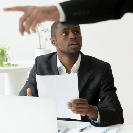 Frustrated shocked African American worker being fired, holding dismissal notice, while Caucasian employer pointing at door asking to leave. Concept of racial discrimination, employment termination