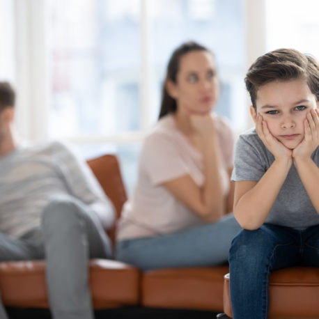 Upset little preschool child boy looking at camera feel sad hurt about parents fights conflicts sit on sofa at home, depressed school kid son suffer from family argument, children and divorce concept